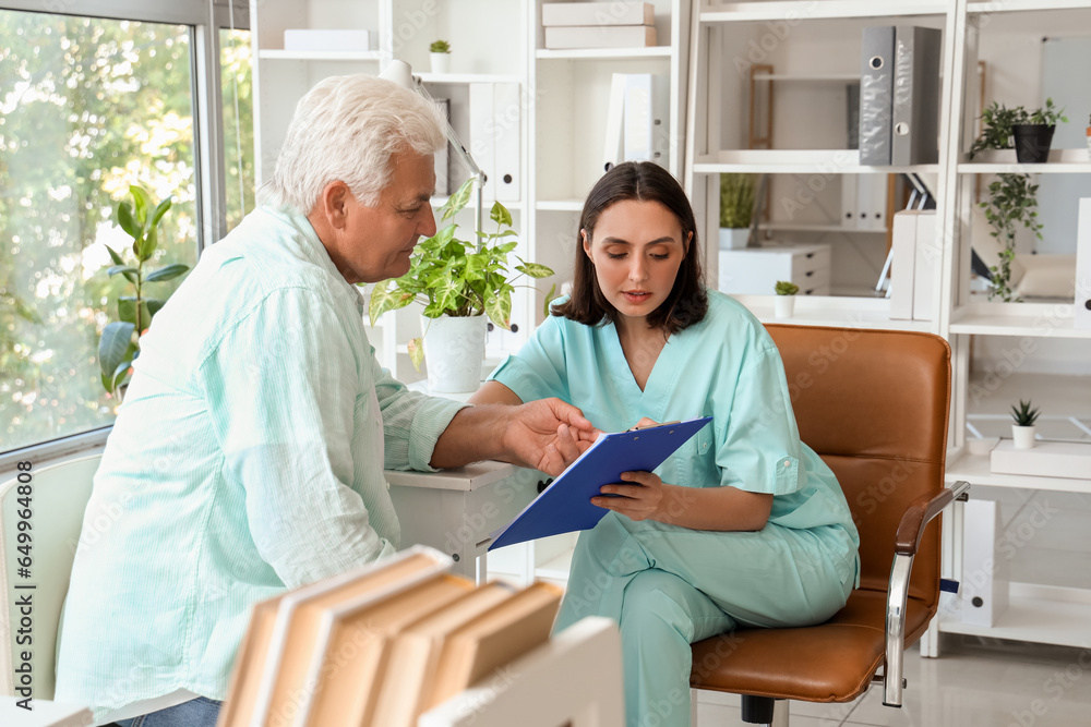 Female doctor showing something on clipboard to senior patient in medical office Female doctor showing something on clipboard to senior patient in medical office