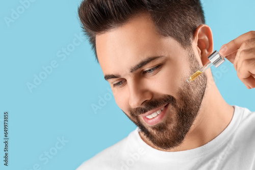 Handsome man applying cosmetic serum onto face on light blue background, closeup. Space for text