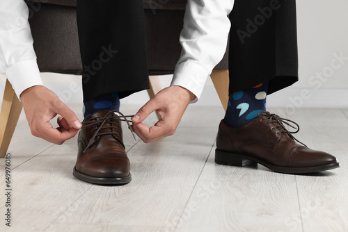 Man with colorful socks putting on stylish shoes indoors  closeup