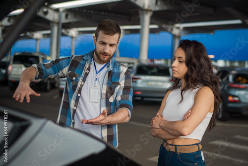 Instructor explaining to young lady about the trunk of a car during studying at a driving school. Driving test, driver courses, exam concept