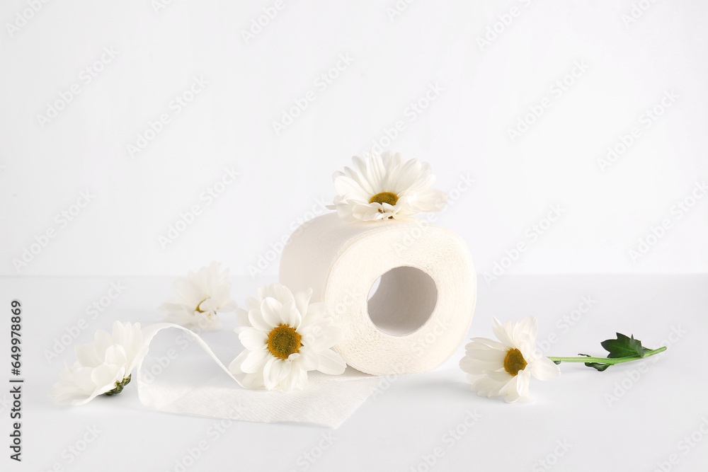 Toilet paper roll with chamomile flowers on white background