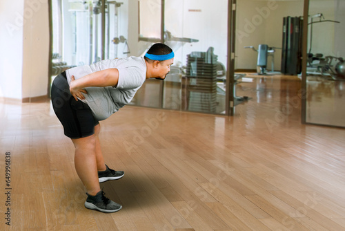 Overweight Asian guy smiling while stretching exercise at gym