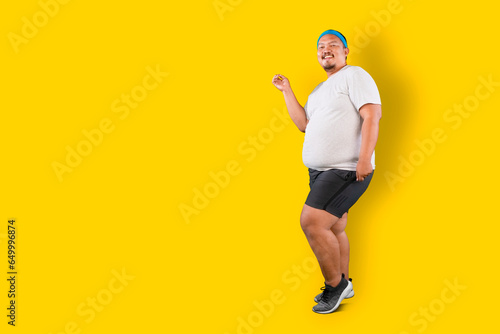 Happy Asian overweight guy dancing isolated over yellow background