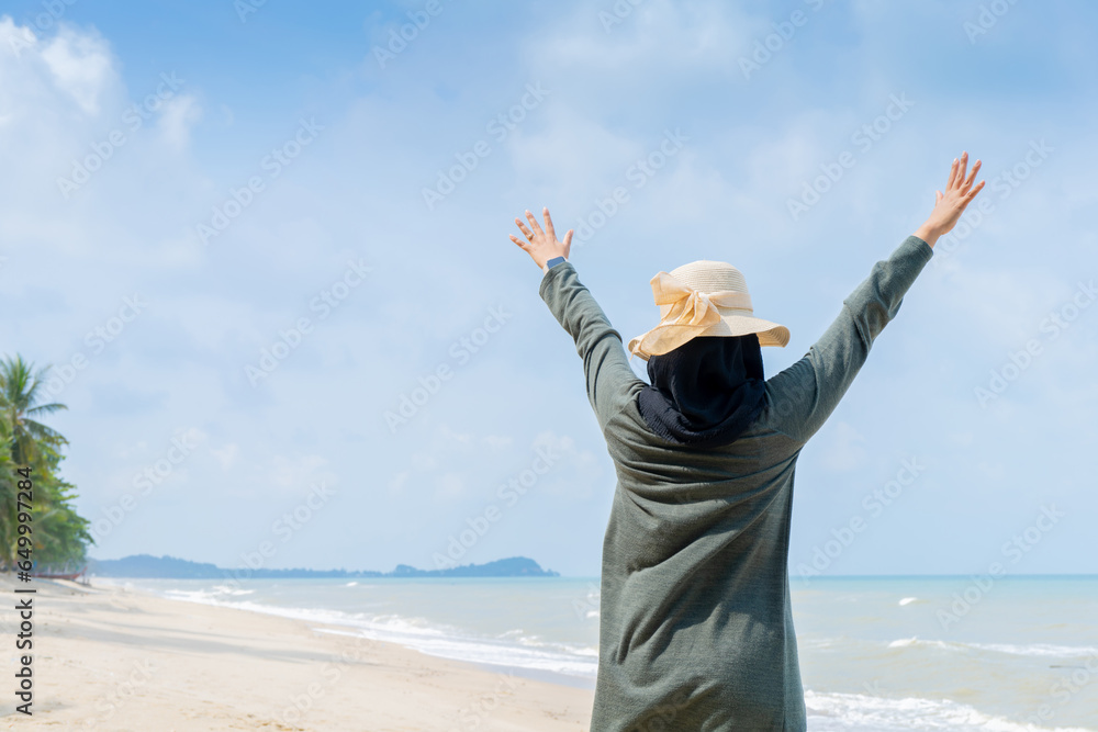 Happy Young muslim woman in grey dress and hat standing on the beach and open hands on sea with breaths a full breast and enjoys freedom. Happy Young muslim woman in grey dress and hat standing on the beach and open hands on sea with breaths a full breast and enjoys freedom.