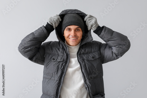 Young man in warm puffer jacket on light background