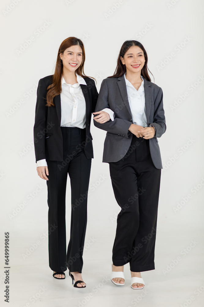 Portrait isolated cutout studio full body shot two Asian professional successful female businesswomen in formal suit standing smiling holding arms smiling together look at camera on white background Portrait isolated cutout studio full body shot two Asian professional successful female businesswomen in formal suit standing smiling holding arms smiling together look at camera on white background