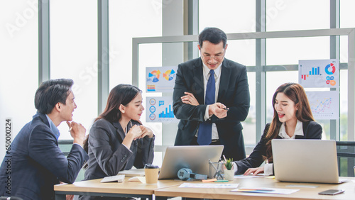 Asian professional successful businessman manager entrepreneur in formal suit standing teaching brainstorming marketing strategy with male female businesswomen employees team in company meeting room
