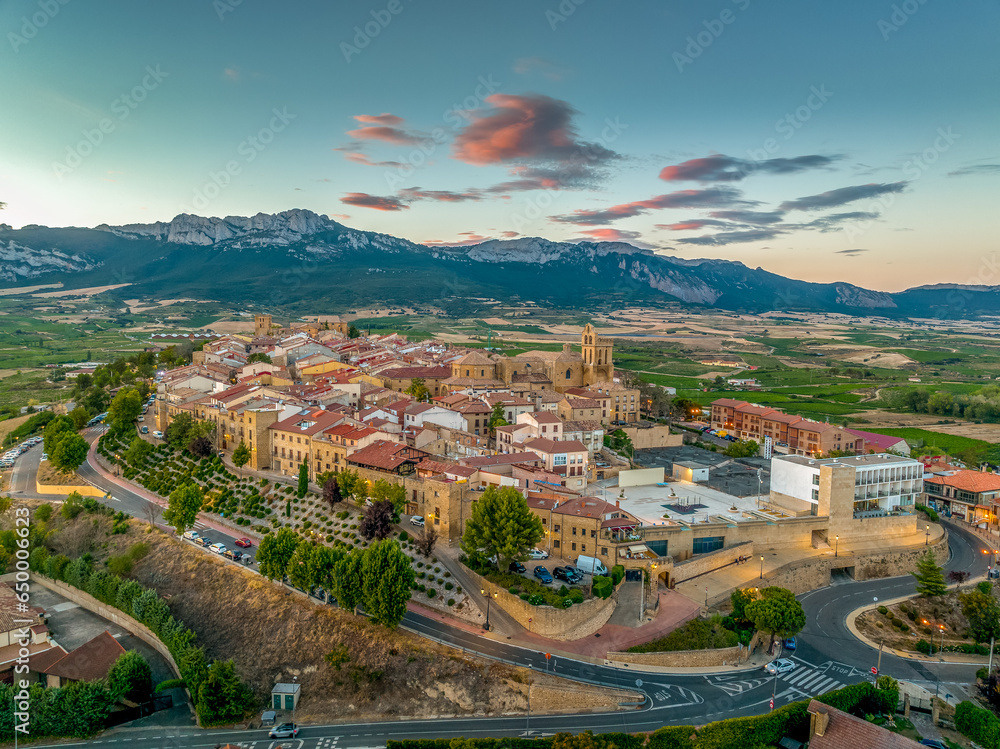 Aerial view of Laguardia medieval fortified hilltop village surrounded by vineries in the Rioja region of Spain, with colorful sunset sky