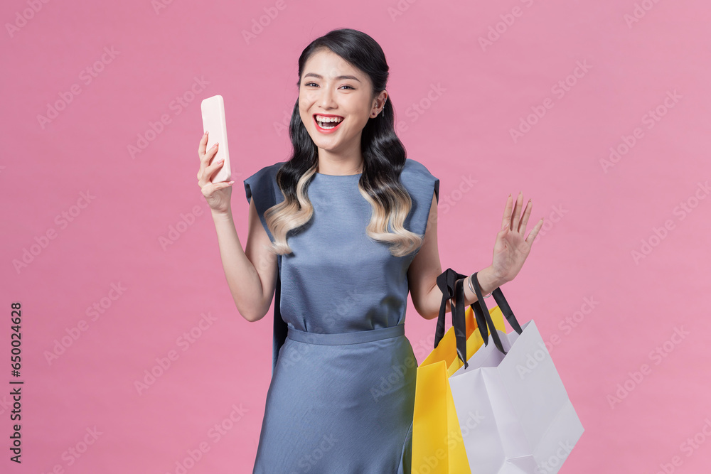 happy young woman holding shopping bags and mobile phone over pink background - obrazy, fototapety, plakaty 