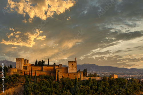 The Alcazaba of the Alhambra in Granada, Spain, illuminated by the warm light of sunset, with a beautiful sky in orange and blue tones in the background