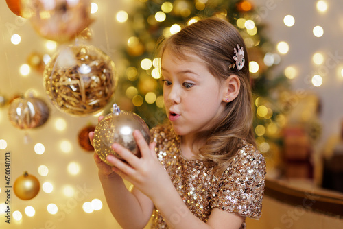 Funny little girl holding golden christmas ball