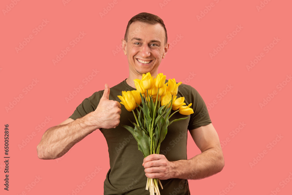 Smiling middle-aged man holding bouquet of yellow tulip flowers and showing thumbs up. Flowers delivery. Pink background. Smiling middle-aged man holding bouquet of yellow tulip flowers and showing thumbs up. Flowers delivery. Pink background.