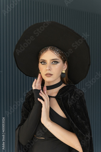 Portrait of a woman with bold makeup wearing a black hat. Beautiful woman dressed in black. Halloween party.
