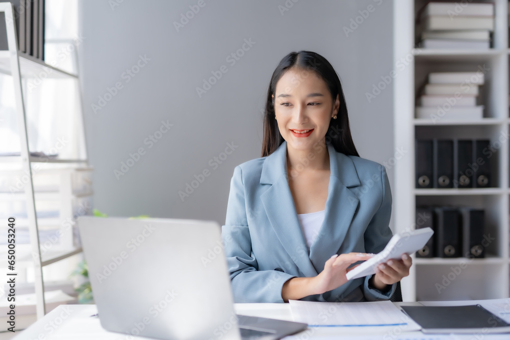 Young Asian businesswoman using a calculator to calculate business principles. Accounting statistics concept at the office. Young Asian businesswoman using a calculator to calculate business principles. Accounting statistics concept at the office.