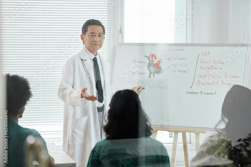Doctor pointing at whiteboard with heart chart when talking to group of medical students