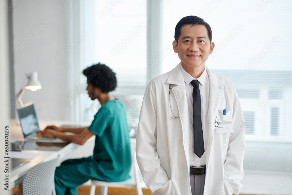 Portrait of smiling general practitioner in labcoat standing in medical office Portrait of smiling general practitioner in labcoat standing in medical office