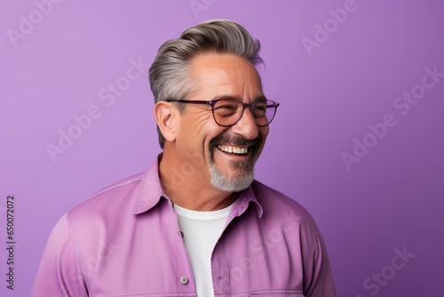 Portrait of happy senior man in eyeglasses laughing and looking at camera while standing against purple background photo