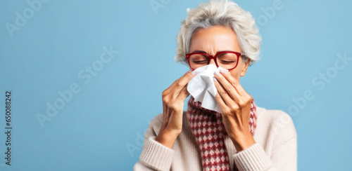 A beautiful senior woman manages her runny nose with elegance, using a pristine white tissue. photo