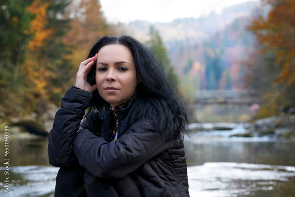 Serious young brunette woman on the bank of an autumn mountain river Serious young brunette woman on the bank of an autumn mountain river