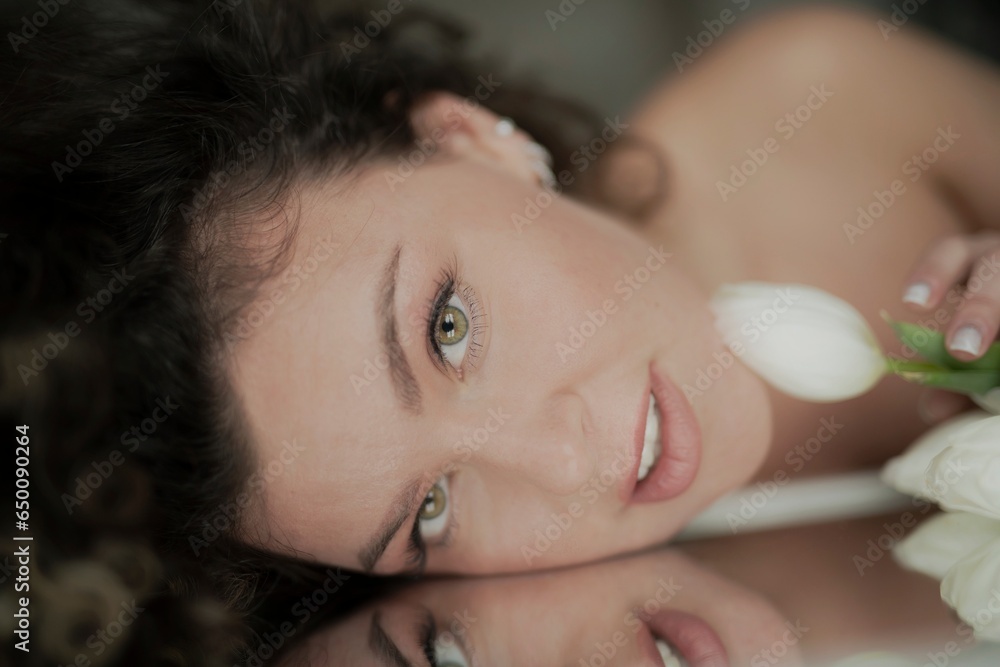 A beautiful young woman lies on a mirror, with a bouquet of tulips A beautiful young woman lies on a mirror, with a bouquet of tulips
