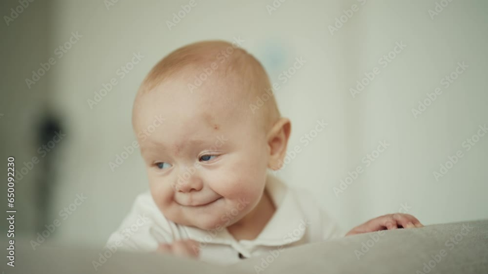 Happy healthy active curious little baby trying to crawling on couch at home and falling. Child smiling looking at camera lying on sofa. First baby's movements, growth development of kid concept. Happy healthy active curious little baby trying to crawling on couch at home and falling. Child smiling looking at camera lying on sofa. First baby's movements, growth development of kid concept.