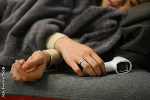 Sick woman holding digital thermometer while lying on couch with fever. Healthcare concept