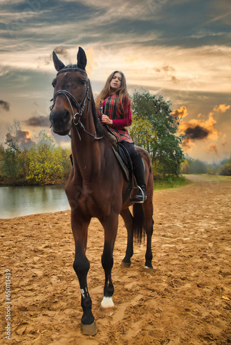 Full length of adult lady on horseback in fall forest by dramatic sky. Rider woman sitting on her horse in autumn park, rural scene. Concept of leisure activity and recreation. Copy ad text space © Alex Vog