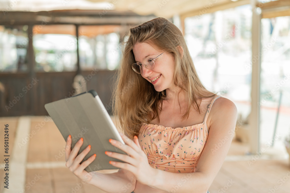 Young French girl with glasses at outdoors holding a tablet with happy expression Young French girl with glasses at outdoors holding a tablet with happy expression