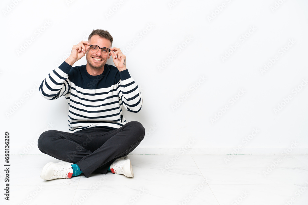Young man sitting on the floor isolated on white background with glasses and surprised Young man sitting on the floor isolated on white background with glasses and surprised