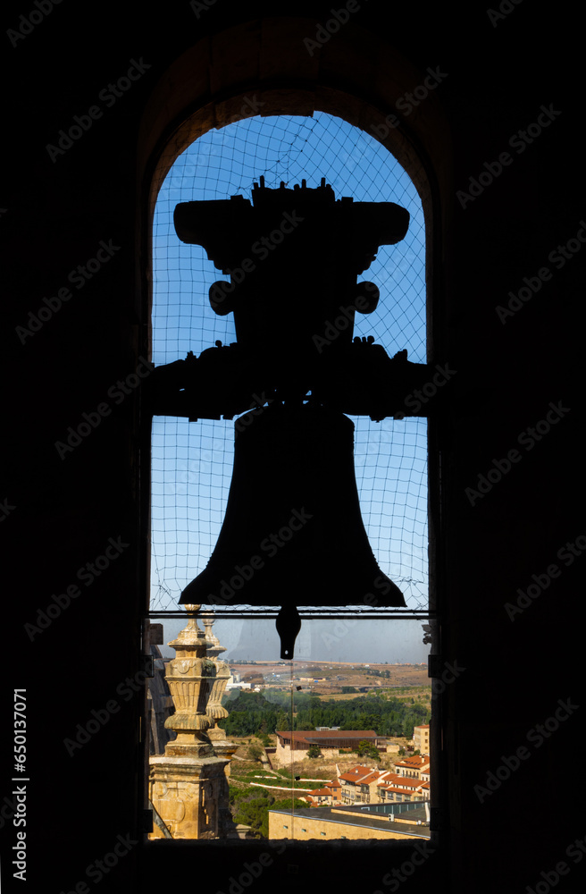 Obraz premium Backlit silhouette of the bronze bell of the old cathedral with the view of the city and mountains of Salamanca from the church tower. Protected with an anti-pigeon mesh.