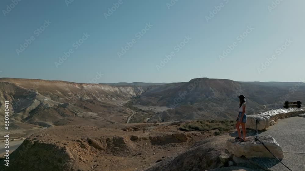European woman stands against the background of the Negev Desert in Israel is visible in the background over mountains, sandy hills and rock formations. European woman stands against the background of the Negev Desert in Israel is visible in the background over mountains, sandy hills and rock formations.