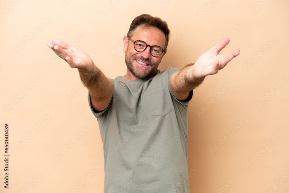 Fototapeta premium Middle age caucasian man isolated on beige background presenting and inviting to come with hand