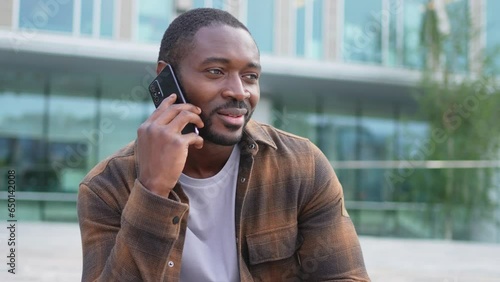 African american man talking on smartphone on street in city outdoor. Man with cell phone chatting with friends. Smiling person making answering call by cellphone. Guy having conversation by mobile
