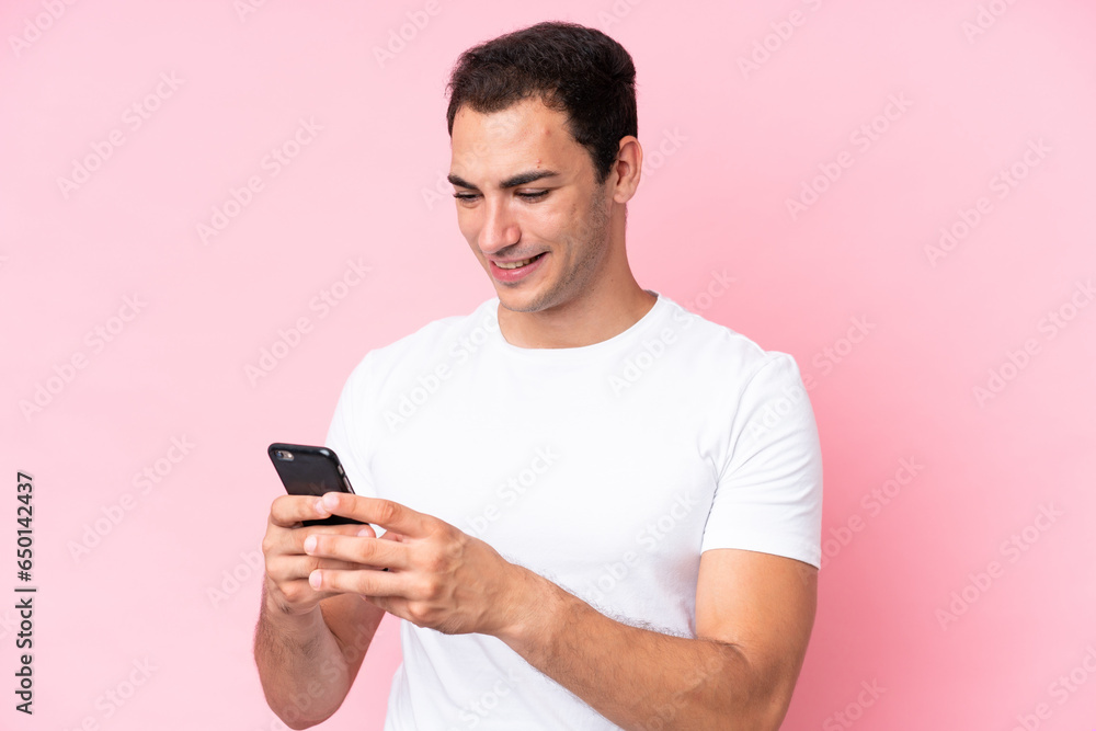 Young caucasian man isolated on pink background sending a message or email with the mobile Young caucasian man isolated on pink background sending a message or email with the mobile