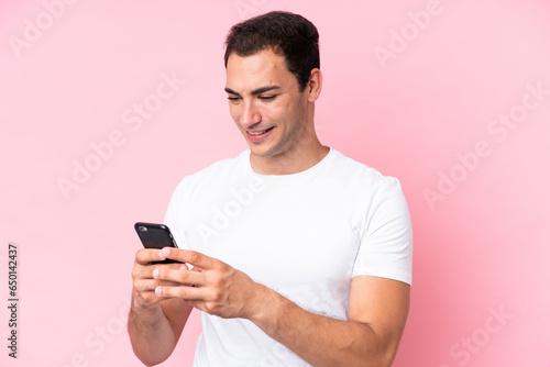 Young caucasian man isolated on pink background sending a message or email with the mobile © luismolinero