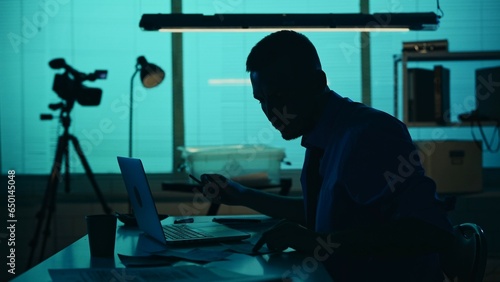 Photos Medium silhouette shot of a detective, policeman sitting in the interrogation room, smoking, working on a laptop and studying the evidence