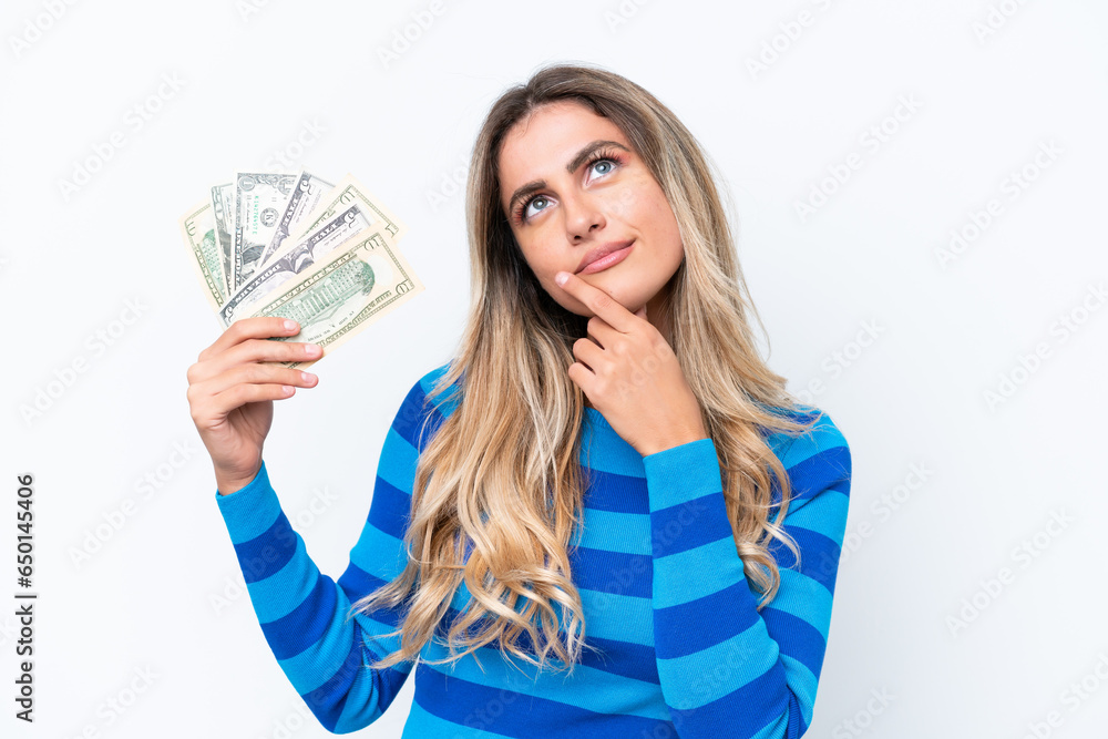 Young Uruguayan woman taking a lot of money isolated on white background having doubts while looking up Young Uruguayan woman taking a lot of money isolated on white background having doubts while looking up