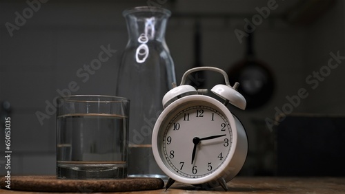 Alarm clock, a glass and a bottle of water on dark background, conceptual photo, reminder to drink water to replace body fluids