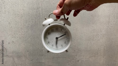 A man's hand holds a ringing alarm clock  on a grey background. Rise, the beginning of the working day.. Rise, the beginning of time to start activities. 