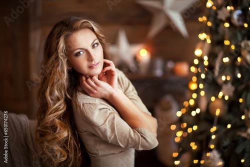 Beautiful young girl with long curly hair standing on a christmas background with boke lights. Magic warm new year photo.