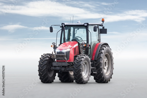 Red modern wheeled tractor isolated on bright background with sky