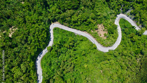 Aerial view of a winding road in the jungle. A concrete road with sharp turns passes through green trees in the forest.