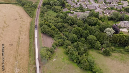 Descending aerial shot tracking steam train travelling into English countryside past a small town photo