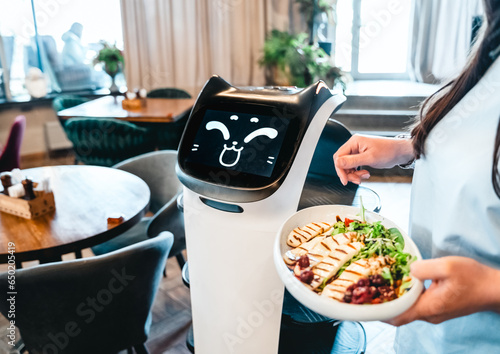 Robot waiter serve food at modern restaurant table.Offering innovation futuristic high-tech automated dining experience.Bringing,delivery automation order to customer.Digital robotic AI smart service
