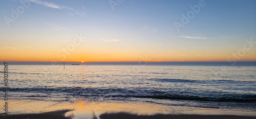 Wide view of a colorful sky over the North Sea where the sun is just setting behind a bank of clouds