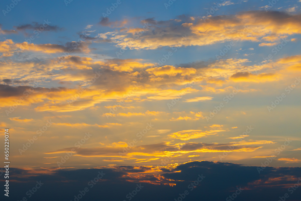 Golden clouds in a blue dramatic sky. The clouds glow golden due to the setting sun. Bright heaven background