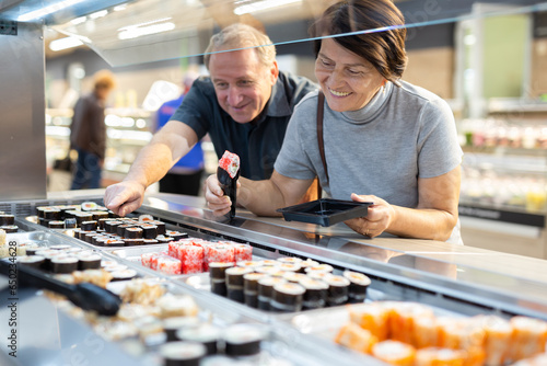 Couple chooses sushi near refrigerator in supermarket