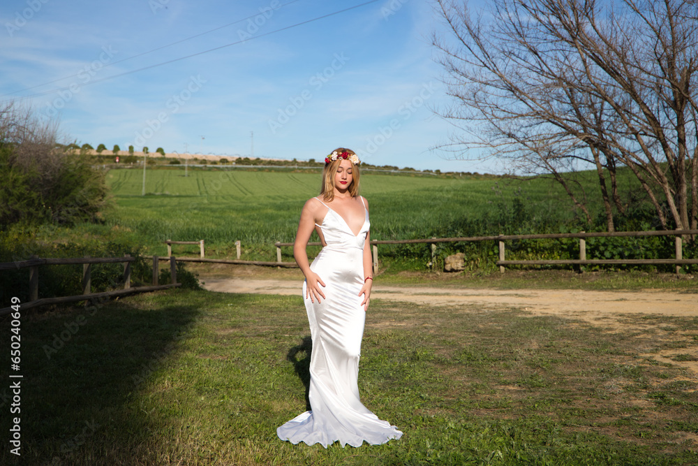 A beautiful young woman, blonde and with long hair, wearing a white dress and a crown of flowers in her hair, is in a field. In the background a green wheat field. The woman is in different poses. A beautiful young woman, blonde and with long hair, wearing a white dress and a crown of flowers in her hair, is in a field. In the background a green wheat field. The woman is in different poses.