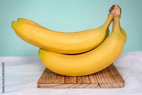 A bunch of bananas on a wooden cutting board (ID: 650243098)