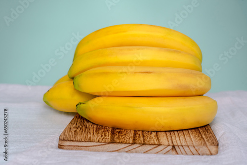 A bunch of bananas on a wooden cutting board (ID: 650243278)